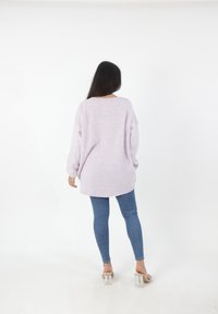Overmaatse lila trui met lange mouwen en een ronde zoom, gecombineerd met slanke blauwe jeans en doorzichtige sandalen met blokhak.