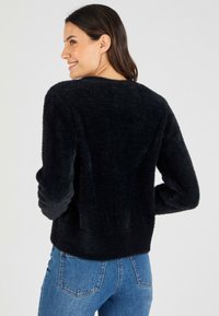 Maglione nero peloso con maniche lunghe e scollo tondo, caratterizzato da una texture morbida e una vestibilità rilassata, abbinato a jeans blu.