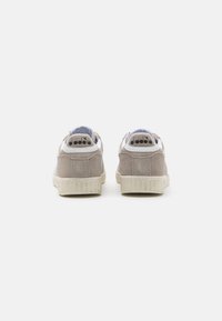 Gray suede sneakers feature a white accent at the heel and a textured cream sole, with perforations and branding at the back.