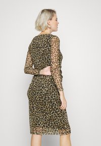 Vestido de padrão de leopardo feito de tecido transparente. Mangas longas, cintura justa, comprimento até ao joelho. A paleta de cores apresenta castanhos, pretos e bejes.