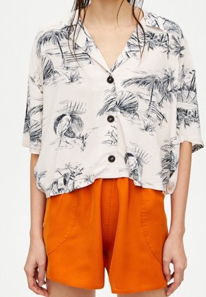 Korte mouwen, ivoorkleurig shirt met zwart palmbomen- en vogelprint, voorzien van een knoopsluiting aan de voorkant en een relaxte pasvorm, gecombineerd met feloranje shorts.
