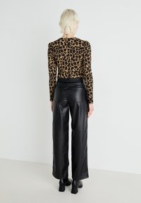 Haut à manches longues imprimé léopard avec épaules rembourrées, associé à un pantalon large en simili cuir noir taille haute et des bottes à talons épais.
