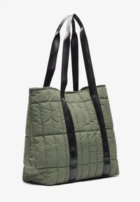 Quiltepurse i olivengrønn med svarte, teksturerte stropper. Designet har et romslig indre og en strukturert form.