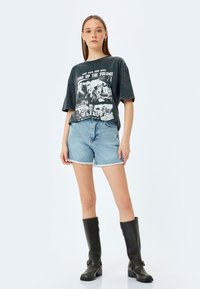 Sort grafisk t-shirt med afslappet pasform, med hvidt tryk og korte ærmer. Kombineret med slidte denimshorts og sorte knæhøje støvler.