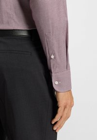Chemise à carreaux rouges et blancs à boutons, avec une texture douce, associée à un pantalon noir sur mesure, affichant un design formel élégant.