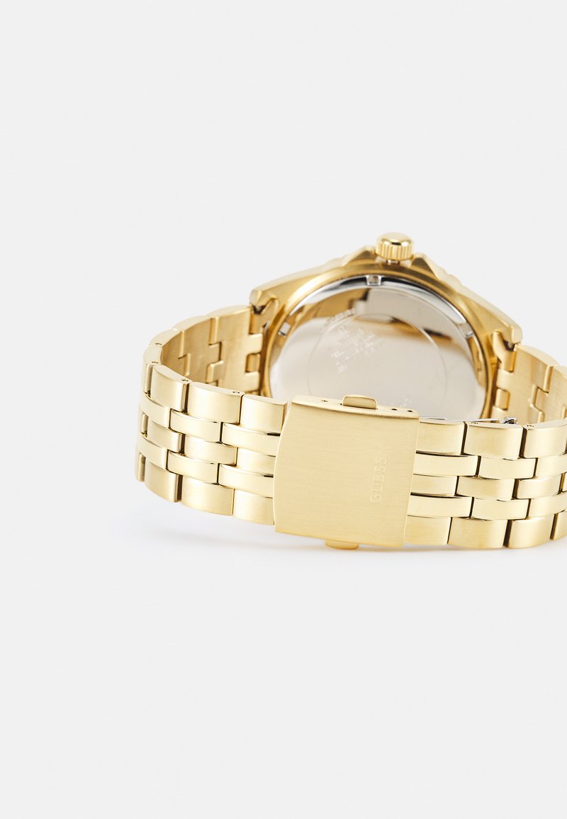 Reloj de pulsera de metal dorado con pulsera de eslabones, caja redonda y fondo de acero inoxidable. Presenta un cierre y un diseño minimalista en la esfera.