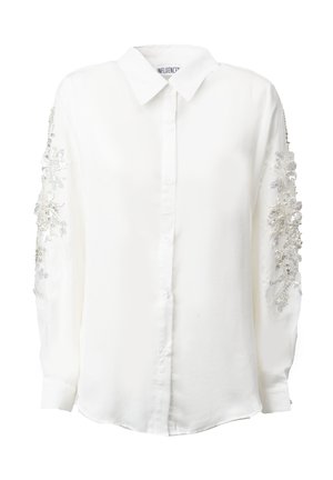 Chemise blanche à manches longues avec des broderies florales argentées et des accents de perles sur les manches. Col classique et coupe ajustée.
