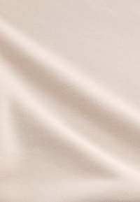 Nærbillede af lys beige stof med subtile diagonale folder og fin vævet tekstur.