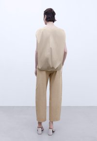 Top beige senza maniche con una vestibilità ampia e dettagli cuciti, abbinato a pantaloni larghi coordinati. L'outfit presenta un design minimalista e linee nette.