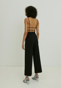 Zwart jumpsuit met spaghetti-bandjes en open rug, met een wijde pijpdesign. Gepaard met lichtblauwe schouderbandjes hakken.