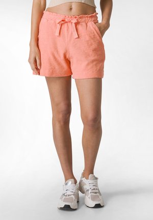 Korallpink frotté shorts med en elastisk talje og snor, med sidelommer og en afslappet pasform. Sammen med hvide sneakers.