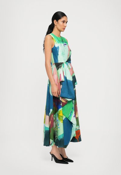 Colorful long dress featuring a mix of green, blue, and pink abstract patterns, with a waist tie and a flowy silhouette, paired with black heels.