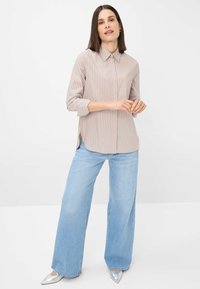 Striped beige blouse with a collar and long sleeves, paired with wide-leg light blue jeans and silver pointed-toe heels.