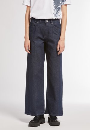 Jeans in denim a gamba larga di colore blu scuro, con vita alta, tasche anteriori e dettagli di cucitura discreti. Abbinati a stivali neri chunky.
