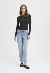 Top negro de manga larga, jeans de mezclilla azul claro de corte holgado y zapatos planos negros, exhibidos sobre un fondo neutro.