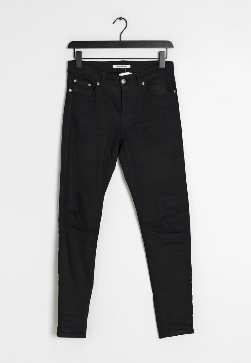 Jeans skinny noirs en tissu extensible, avec un design à cinq poches, des accessoires métalliques et une texture lisse. Accrochés à un cintre noir.
