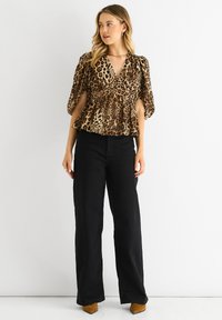 Peplum-Top mit Leopardenmuster und Puffärmeln, kombiniert mit hochtaillierten schwarzen Weiteren Hosen und braunen spitz zulaufenden Schuhen.