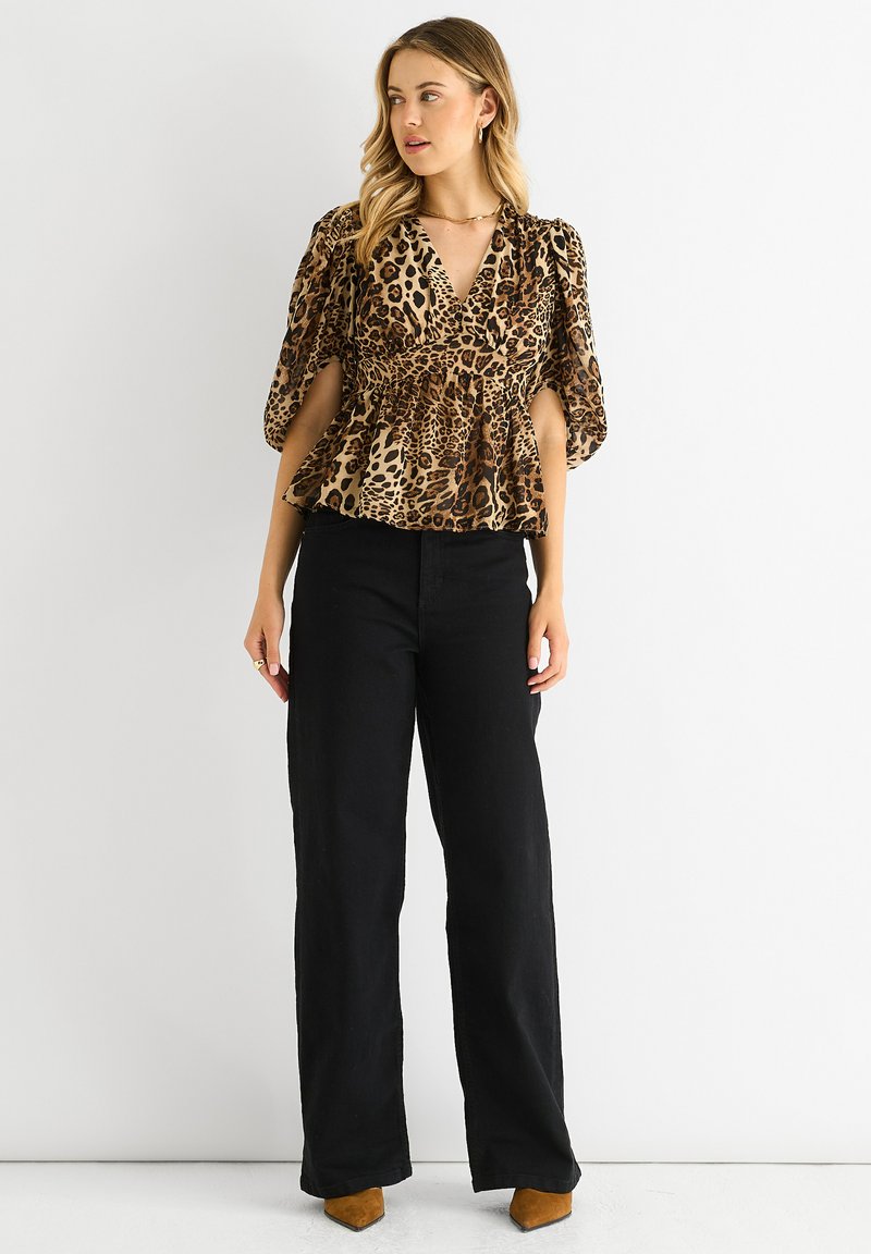 Peplum-Top mit Leopardenmuster und Puffärmeln, kombiniert mit hochtaillierten schwarzen Weiteren Hosen und braunen spitz zulaufenden Schuhen.