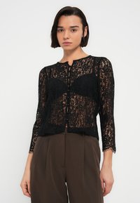 Μαύρη δαντελένια ζακέτα με κομψό κοντό κόψιμο, μανίκια τριών τετάρτων, μπροστινά κουμπιά και λουλουδένιο σχέδιο. Διαθέτει κυματιστό τελείωμα και ελαφρύ υλικό.