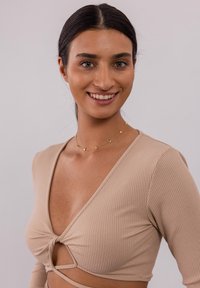 Beige gestreifter Langarm-Top mit tiefem V-Ausschnitt und Knotendetail vorne sowie Ausschnitt. Getragen mit einer zarten Goldkette.