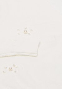 Tessuto di maglia bianco con piccole perle decorative disposte in un motivo circolare sulle maniche. La consistenza è morbida e a maglia allentata.