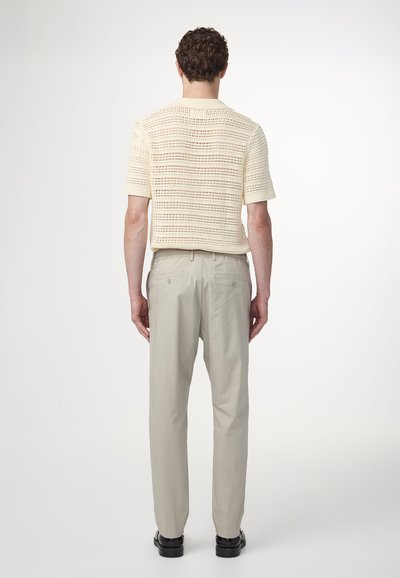 Stickad beige kortärmad topp med ett strukturerat mönster, i kombination med ljusgrå byxor. Skorna har en svart design med en slät yta.