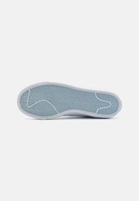 Semelle de sneaker en caoutchouc bleu clair, présentant un motif en chevron pour l'adhérence, un bord blanc lisse, et un design de bout arrondi.