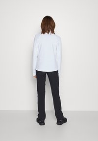 Biała bluzka z długim rękawem o dopasowanym kroju, w połączeniu z czarnymi spodniami. Bluzka ma gładką teksturę i okrągły dekolt.