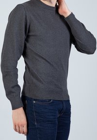 Czarnoszary sweter z dzianiny z okrągłym dekoltem, prążkowanymi mankietami i dołem, dopasowany fason, noszony z ciemnoniebieskimi dżinsami, ukazujący profil boczny.