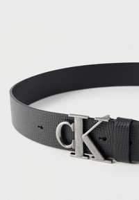 Μαύρη δερμάτινη ζώνη με υφή, διαθέτει αγκράφα σε ασημί απόχρωση με χαραγμένο το λογότυπο "CK". Ρυθμιζόμενη με πολλαπλές τρύπες.