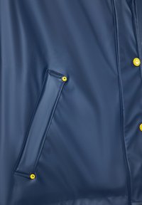 Jūros tamsiai mėlynas vandeniui atsparus švarkas su lygiu paviršiumi, turintis šoninę kišenę ir geltonus spaudimo mygtukus užsegimui.