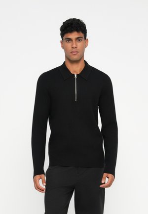 Black knit sweater with a collared neck and a silver zipper, featuring long sleeves and a fitted shape, presented on a model.