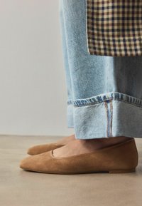Tan ruskind ballet flats med spids tå og lav hæl, parret med lyseblå opbrettede jeans med et ternet stof accent.
