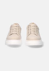 Zapatilla beige con una superficie lisa, cordones texturizados, detalles dorados en los ojales y una suela blanca gruesa para mayor amortiguación.