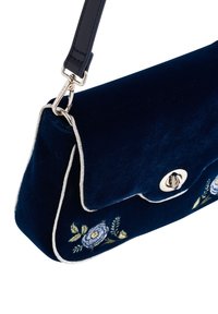 Marinblå sammetväska med broderad blommönster, silverdetaljer och ett lock med magnetisk stängning. Har en avtagbar rem.