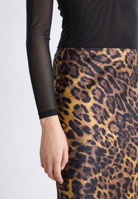 Top de malla negra de manga larga combinado con una falda de estampado de leopardo que presenta tonos dorados y negros, textura suave y un diseño ajustado.