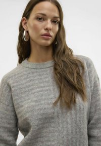Suéter gris claro con un sutil patrón de rayas, hecho de una tela suave, que presenta un escote redondeado y un ajuste ligeramente holgado. Modelo con cabello largo.