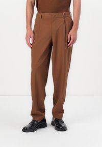 Brown tailored trousers with a straight cut, flat front, belt loops, and side pockets, paired with black shoes on a white background.