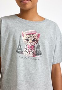 Grå T-shirt med en tecknad leopard som har en rosa makaron och en rosett, omgiven av Eiffeltornet och en byggnad, med texten "Från Paris med kärlek!"