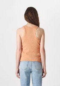 Orange ribbet tank topp med rund hals og racerback design, kombinert med lyseblå høytlivsjeans.