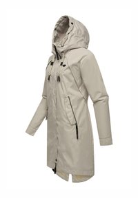 Impermeabile di un leggero beige con cappuccio, chiusura frontale con zip e lacci. Include due tasche con zip e un retro più lungo. Materiale liscio e resistente all'acqua.