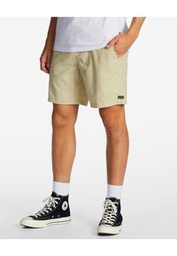 Shorts beige à finition texturée, avec une étiquette noire de marque. Associés à des baskets montantes noires et des chaussettes blanches montantes.