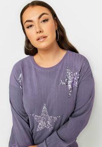 Lila ribbad långärmad topp med silver- och lila paljettstjärndesigner. Mjuk textur med rund halsringning.