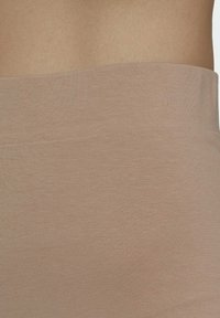 Tissu extensible beige avec une texture lisse et une large ceinture, démontrant un design sans couture et un ajustement près du corps.