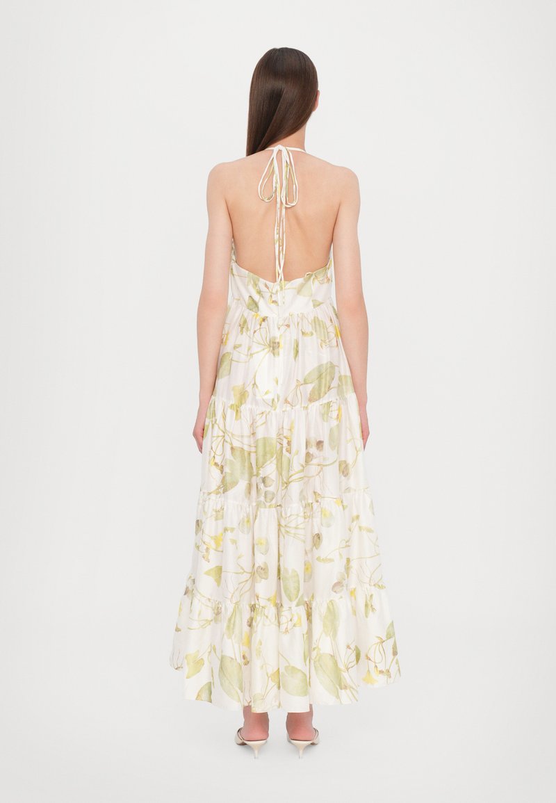 Vista trasera de un maxi vestido con estampado floral y cuello halter, hecho de tela ligera en blanco con diseños en verde y amarillo.