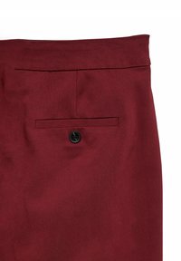 Primer plano de unos pantalones de tela burdeos con un solo bolsillo trasero negro abotonado centrado debajo de la cintura.