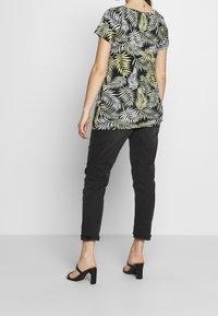 Květinový top s krátkým rukávem s zeleným a bílým vzorem listů na černém pozadí; spárovaný s tmavými skinny džíny a černými sandály na podpatku.