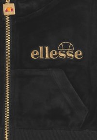 Giacca zip-up in velluto nero con logo "ellesse" ricamato in oro, tasca frontale e hardware della cerniera in oro con finitura testurizzata.