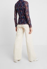 Doorzichtige top met bloemenpatroon in marineblauw en meerdere kleuren, gecombineerd met wijde crèmegekleurde corduroy broek. De textuur is zacht met een gladde afwerking.