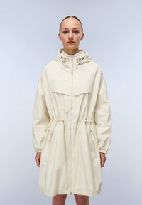 Cappotto impermeabile beige chiaro con cappuccio regolabile, zip completa, due tasche con zip e polsini elasticizzati con un design in vita cinch.